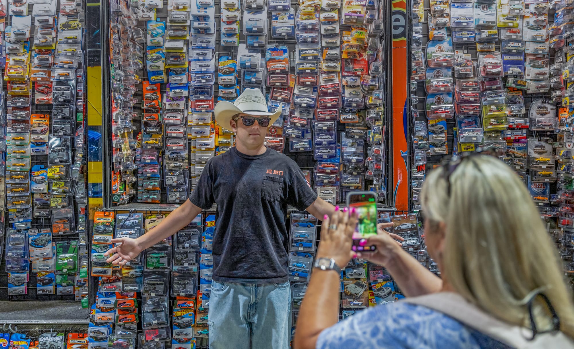 A man in a cowboy hat poses for a photo in front of a wall covered in toy cars.
