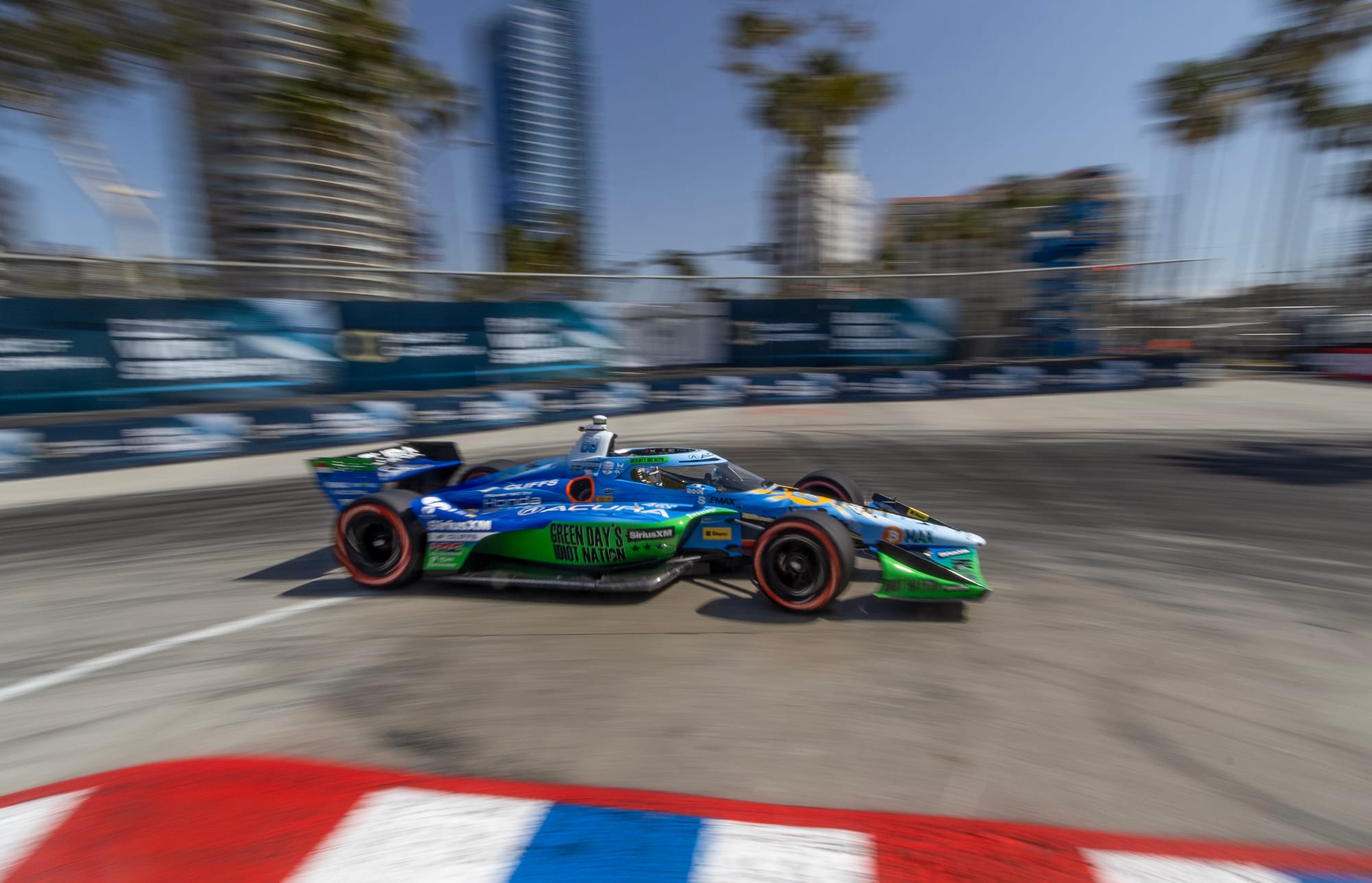 A blue and green race car turns a corner with a blurry background.