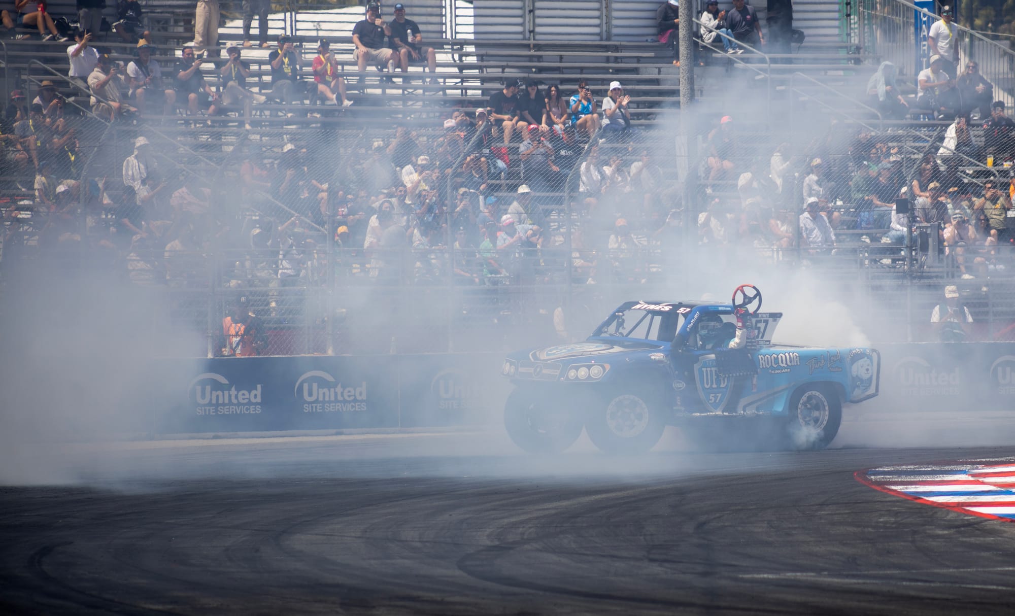 A blue truck kicks up a lot of smoke on a race track.