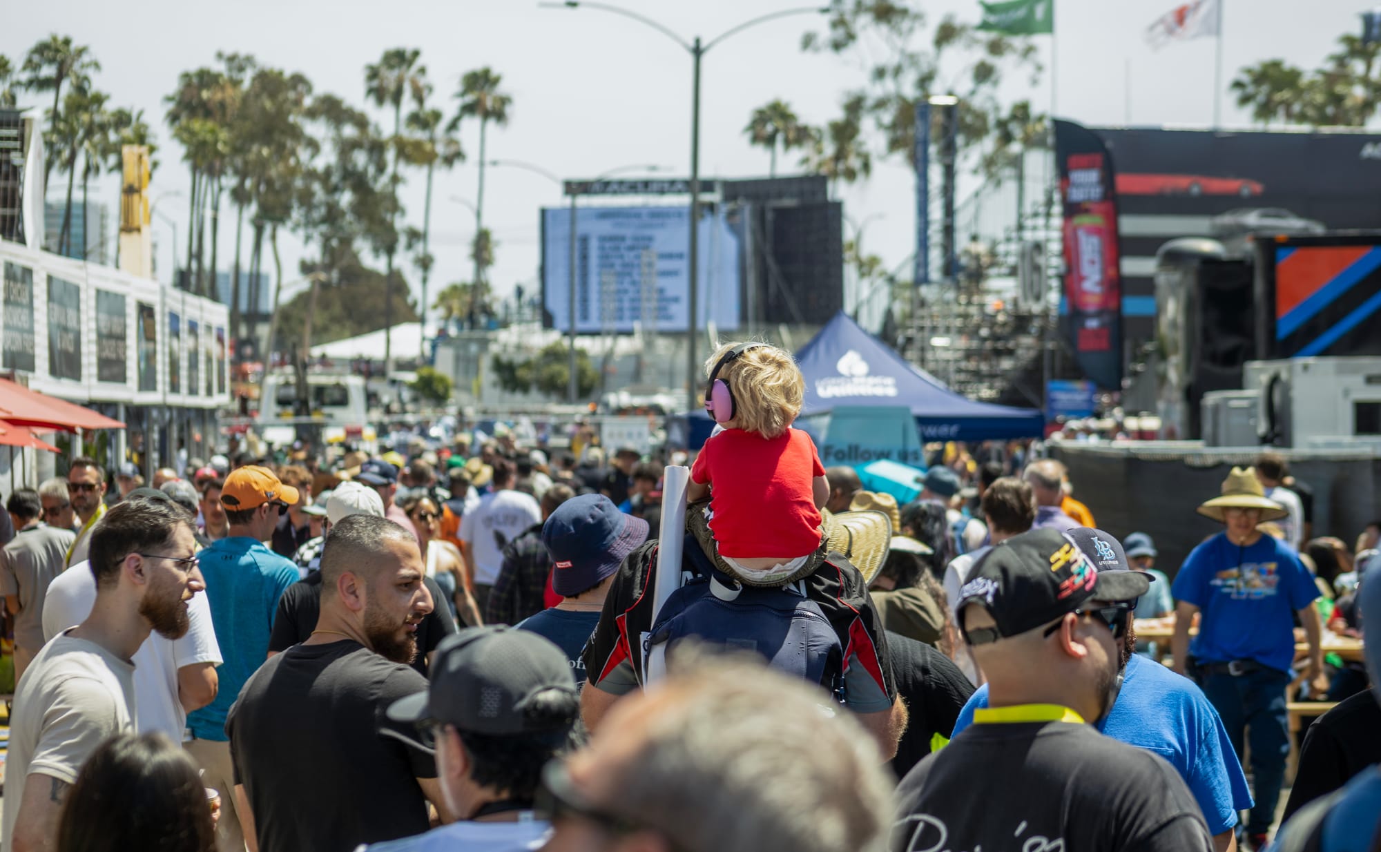 A child sits on an adults shoulders in a large crowd.