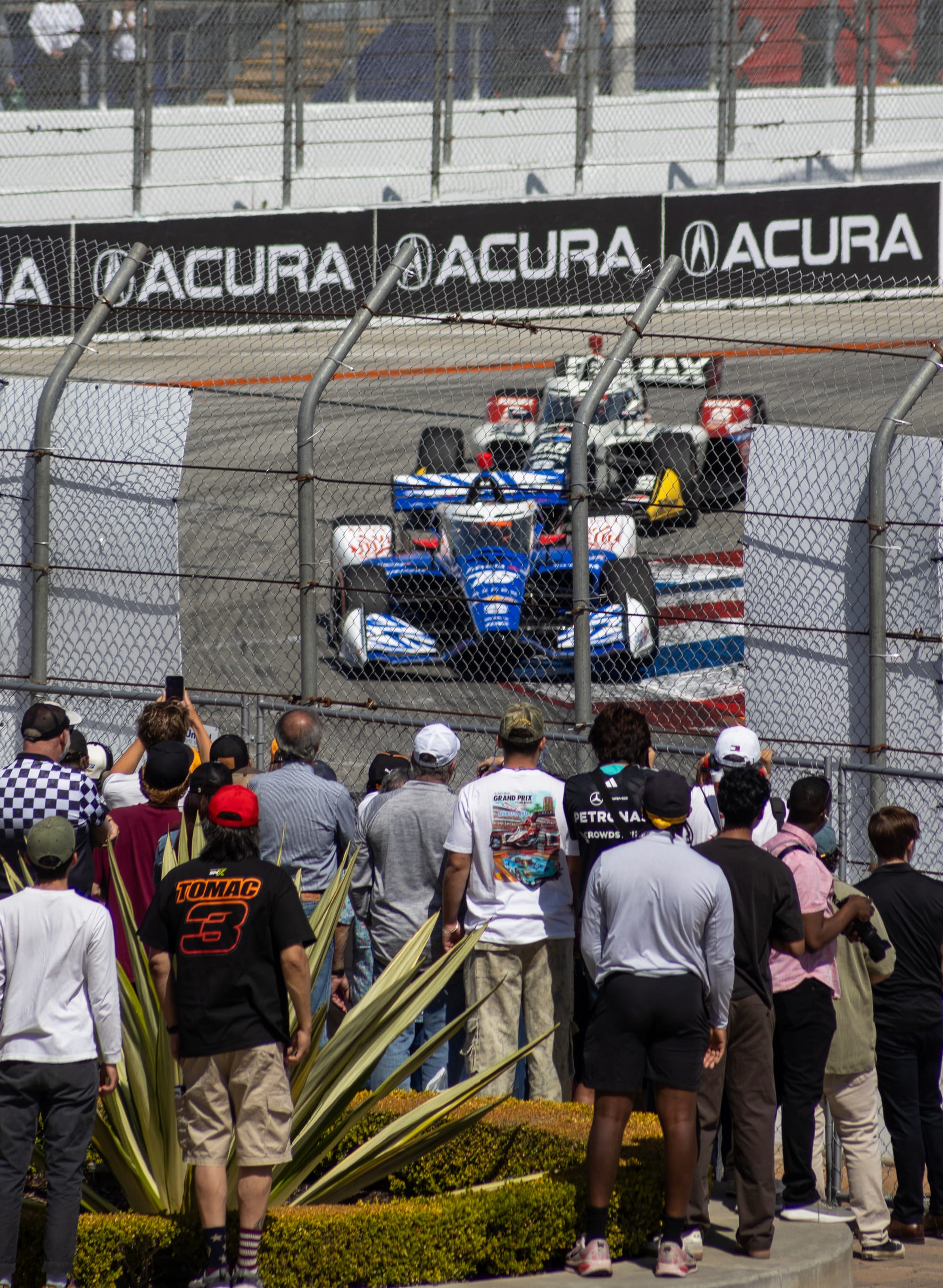 Fans behind a chain link fence watch a race car round a corner.