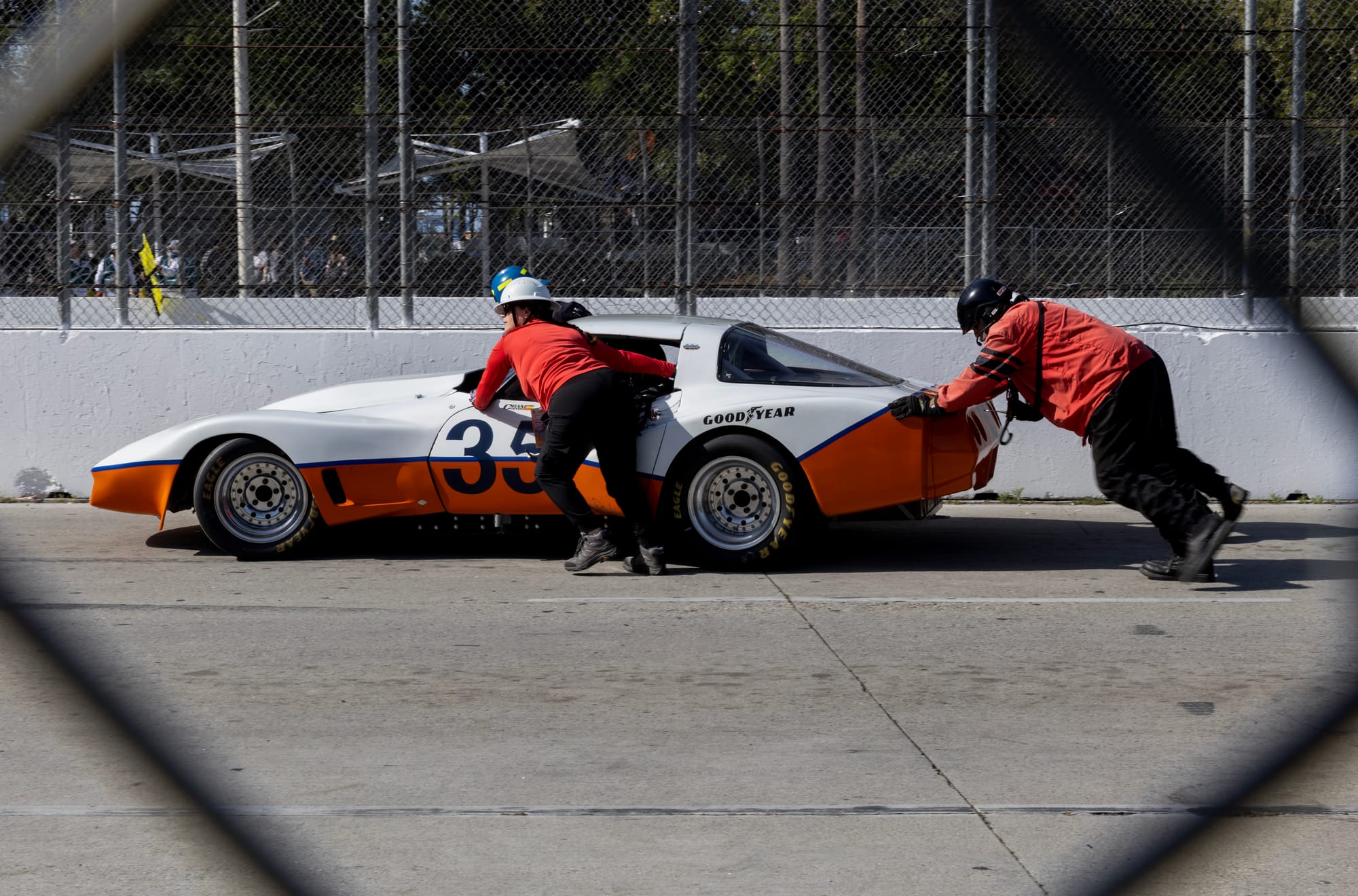 Two people push a red and white car.