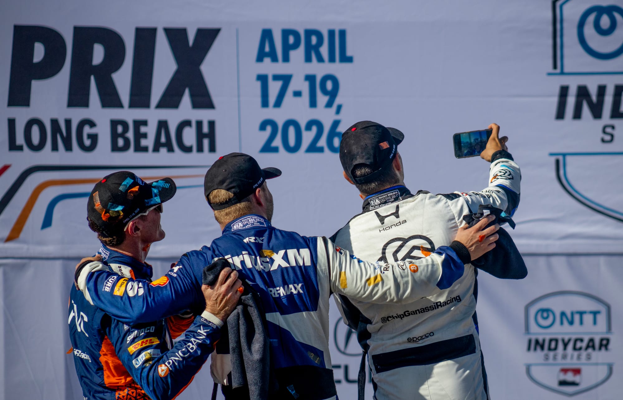 The backs of three men as they pose for a camera selfie.