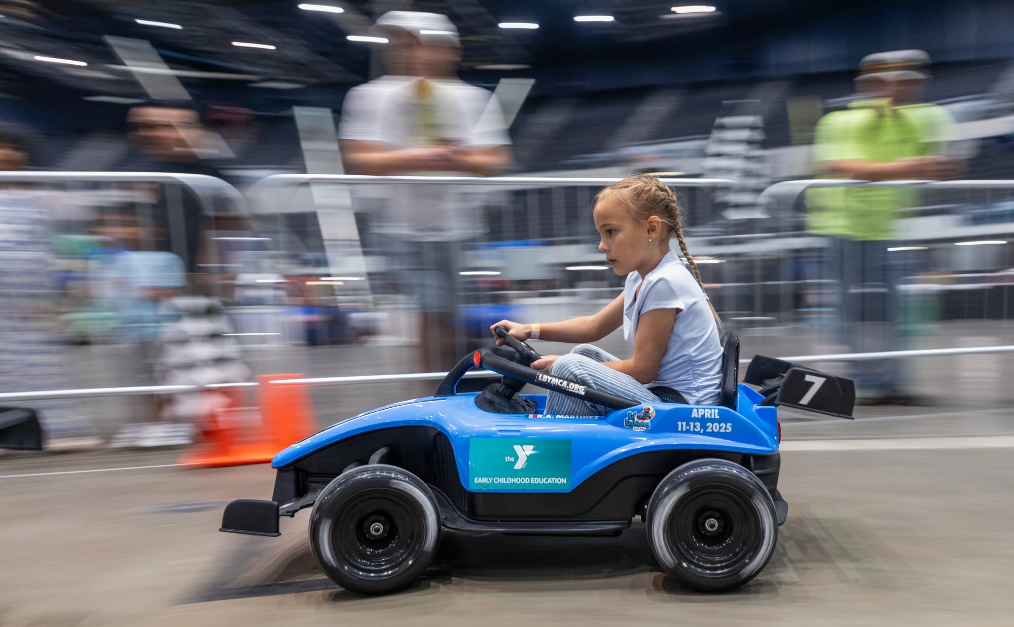 A girl in a small blue car drives on a small race track.