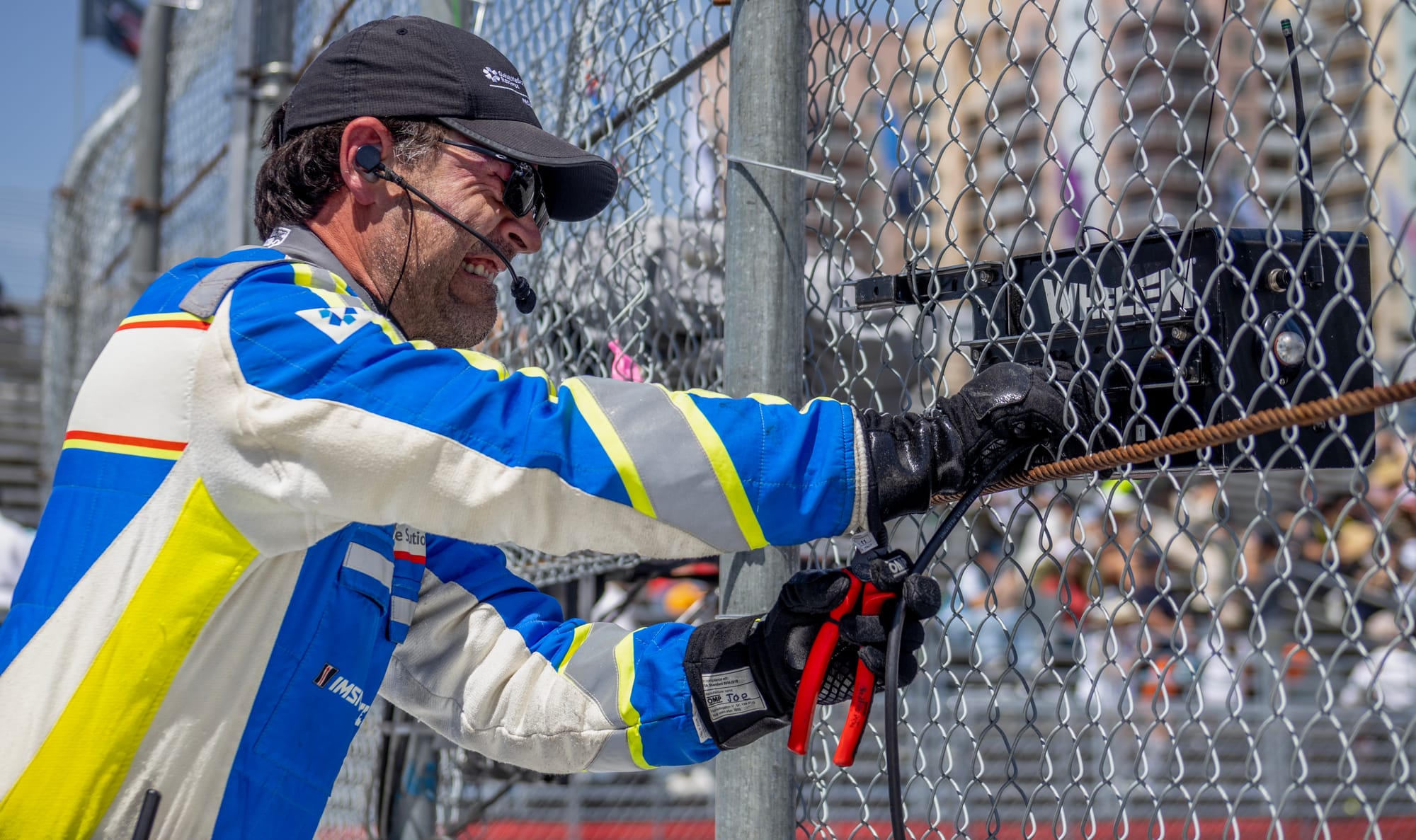 A man struggles with a pair of pliers next to a chain link fence.