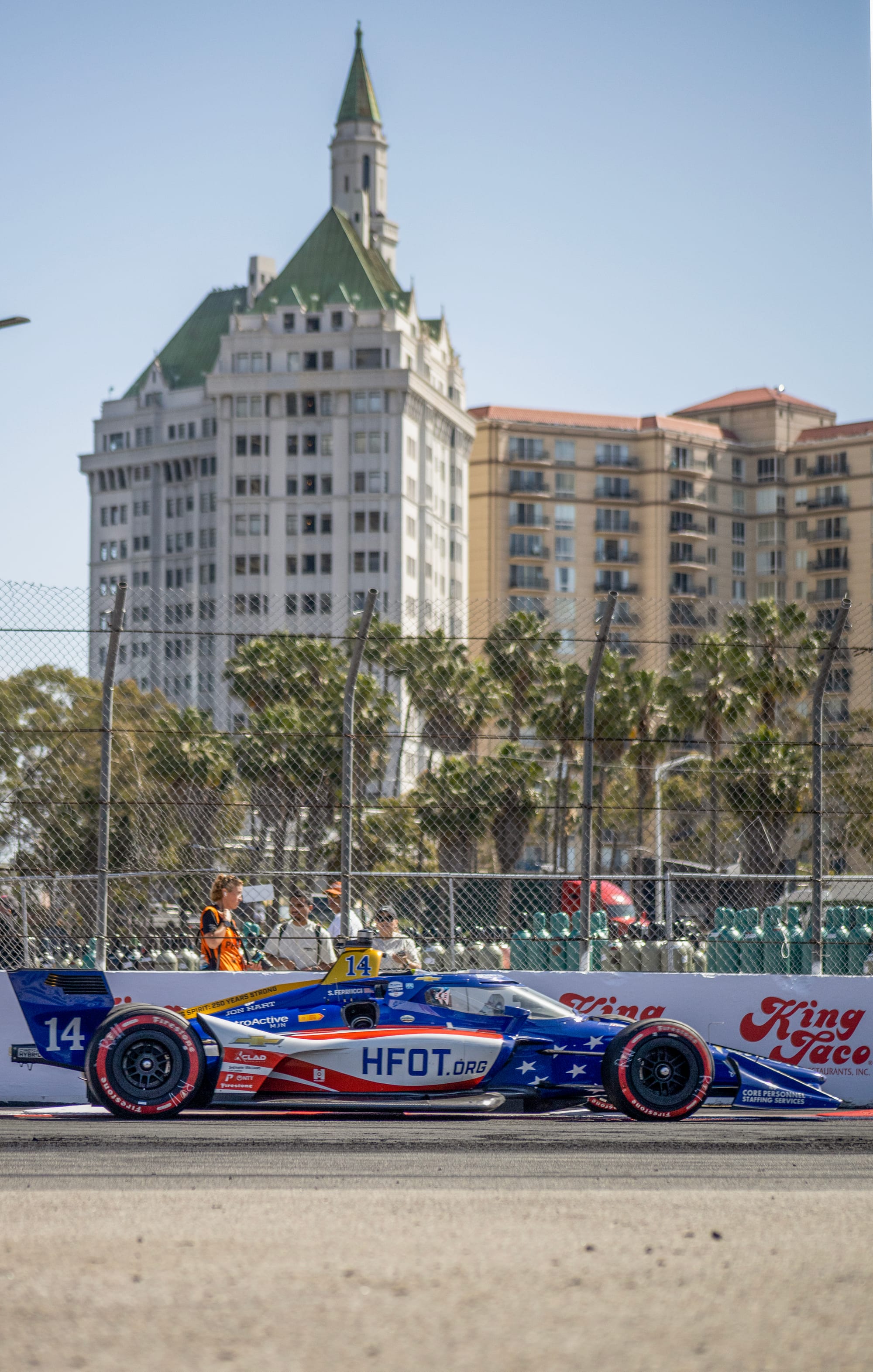 A red, white and blue race car sits parked in front of an old apartment building.