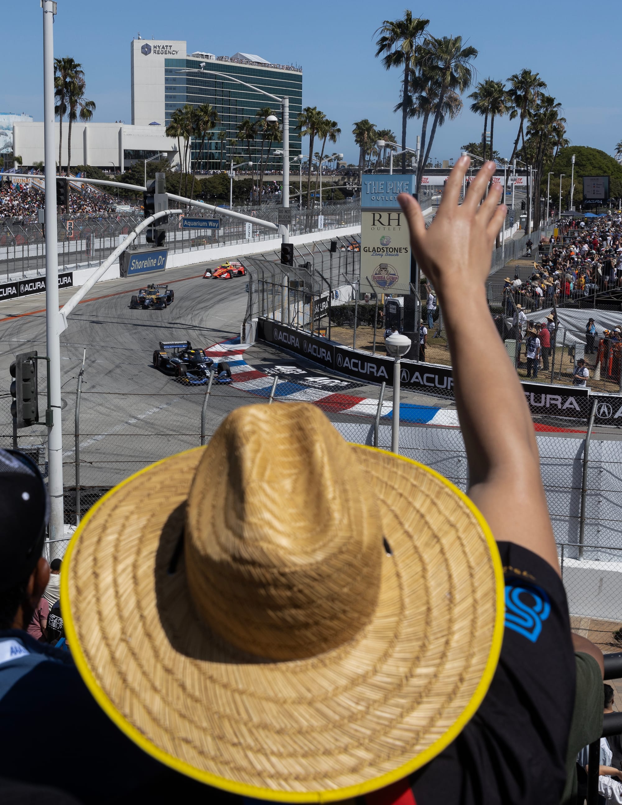 A person in a straw hat waves at race cars.
