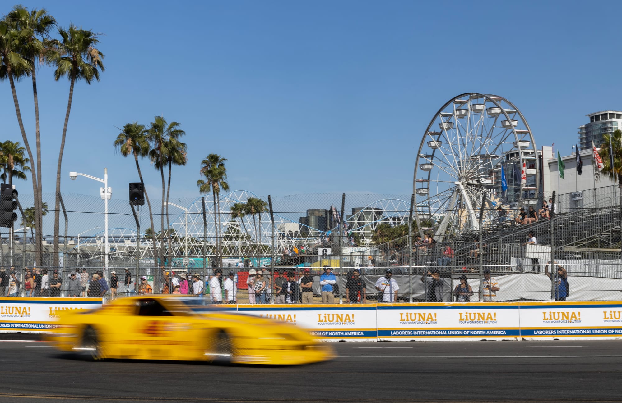 A blurry yellow race car speeds along a race track on a clear day.