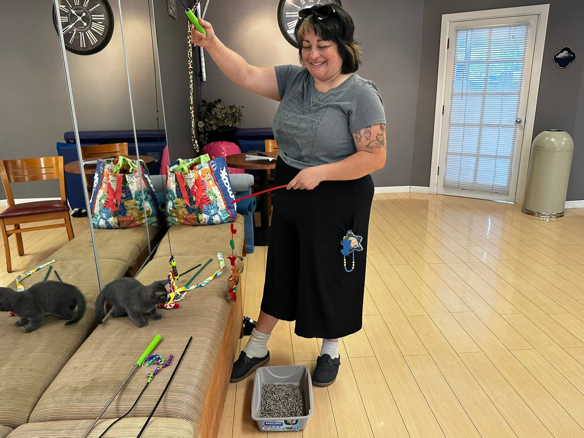 A woman dangles toys in front of a gray kitten perched on a bench.