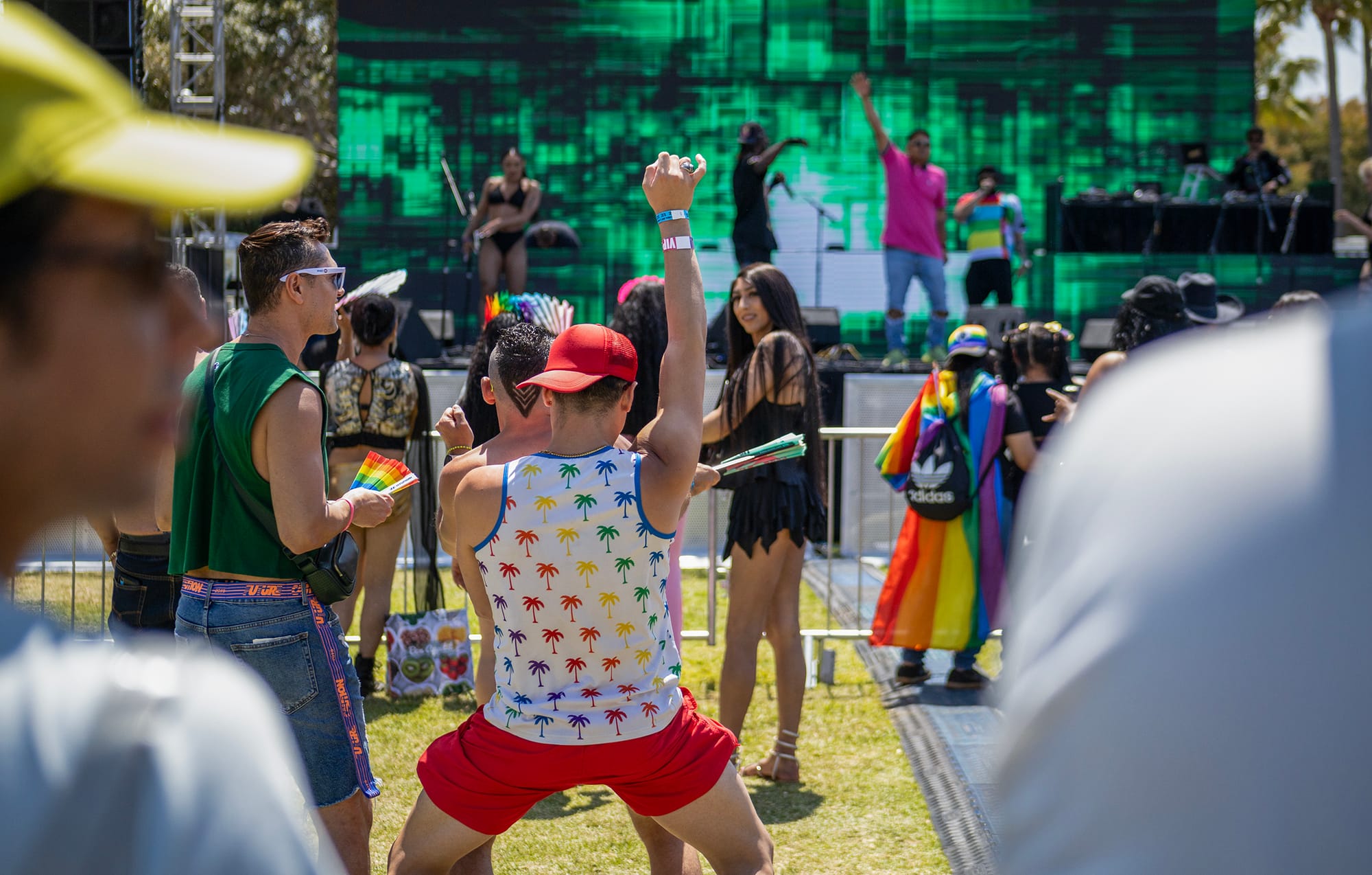 Men and women dance outside in front of a large green stage.