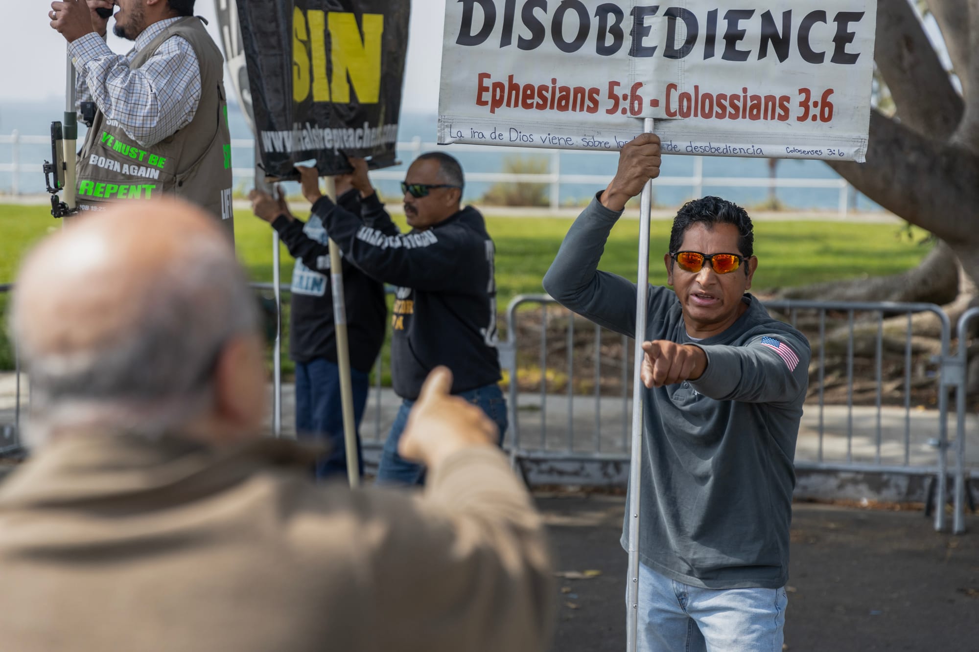 A man argues with other men holding signs saying "Sin" and "Disobedience."