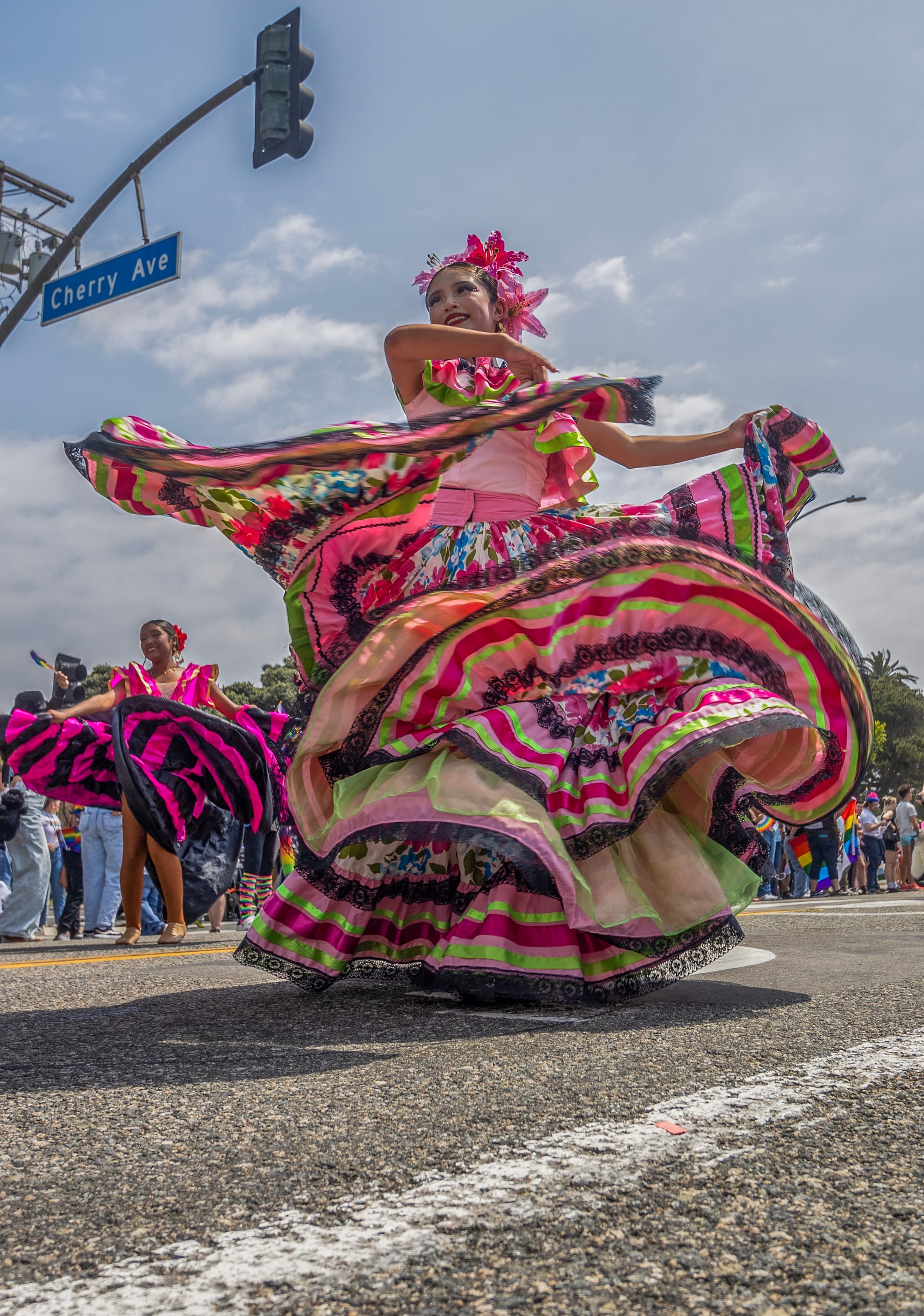 A teen girl in a colorful and elaborate dress dances in the street in front of a large group of people.