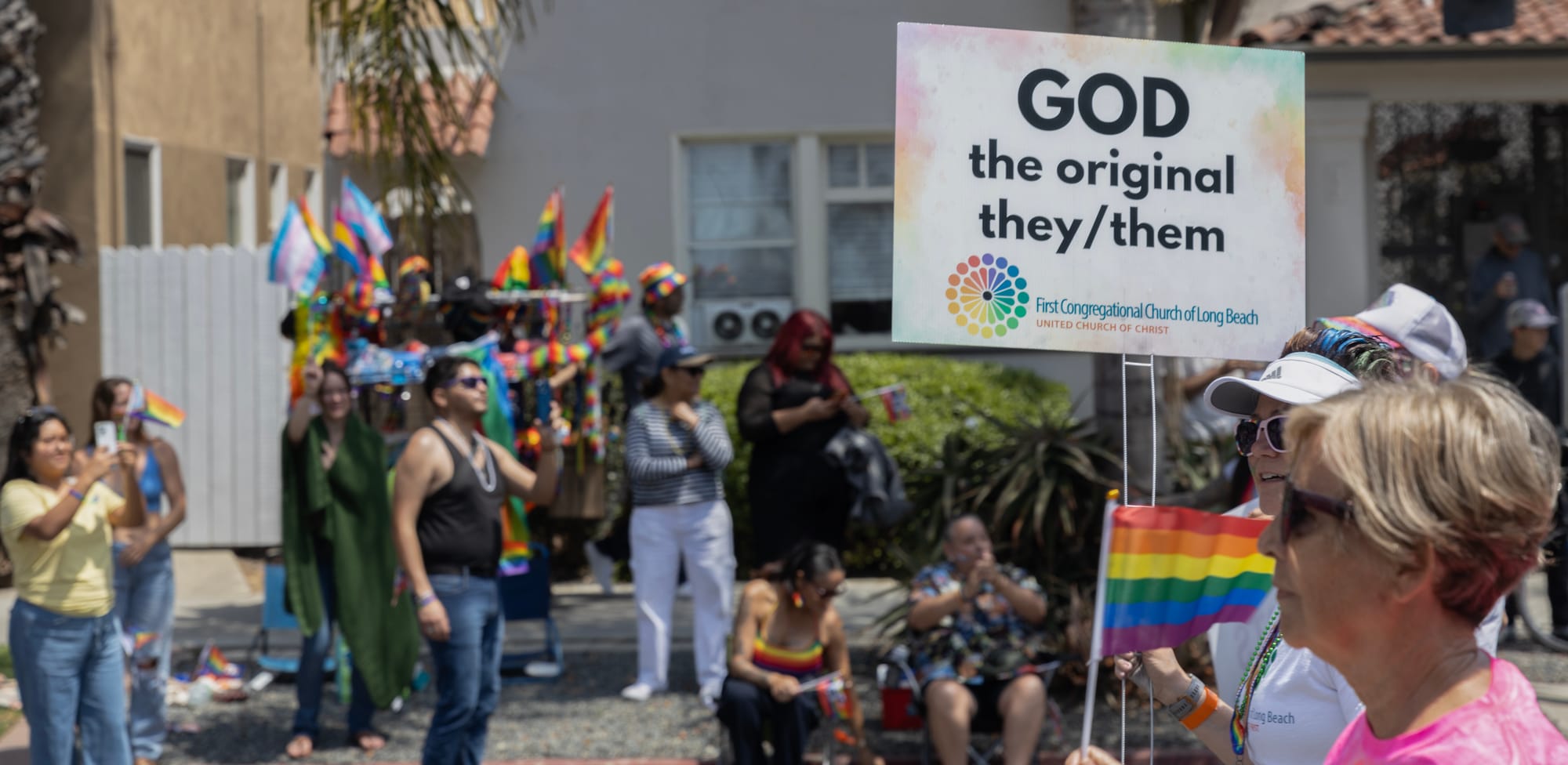 People look on as a person carries a sign saying "God the original they/them."
