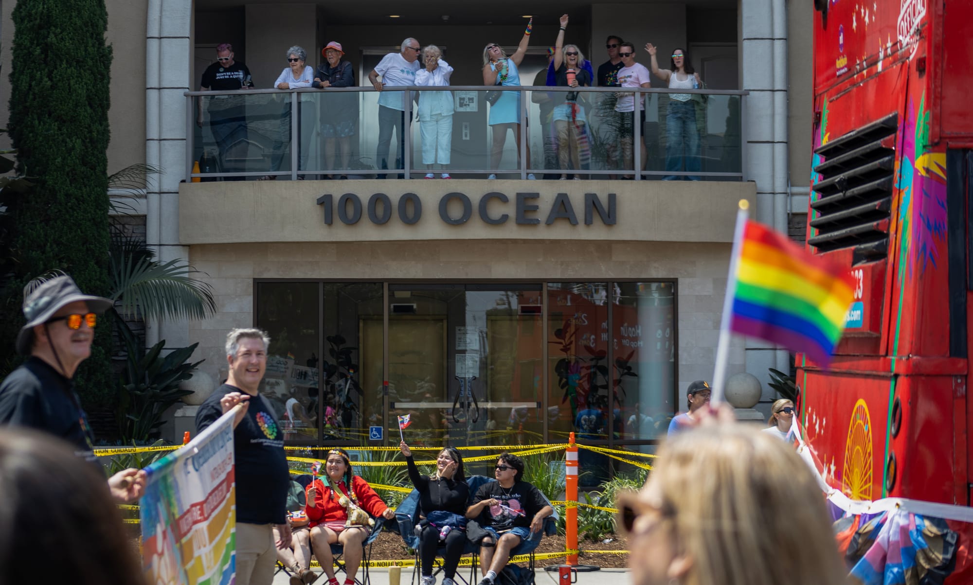 A group of people stand on a balcony of a building labeled "100 Ocean" as people walk past them.