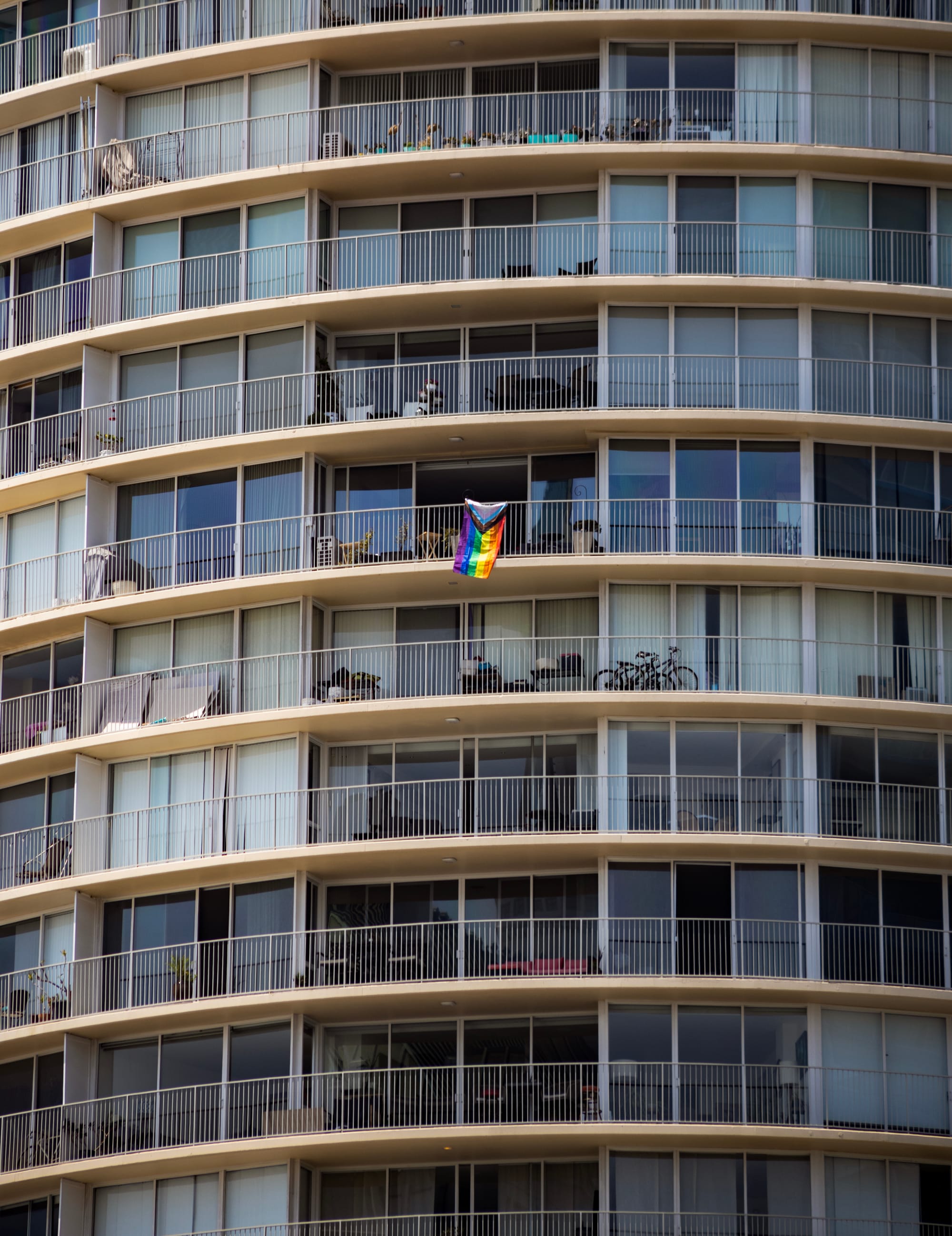 A single rainbow flag hangs off the balcony of a high-rise building.