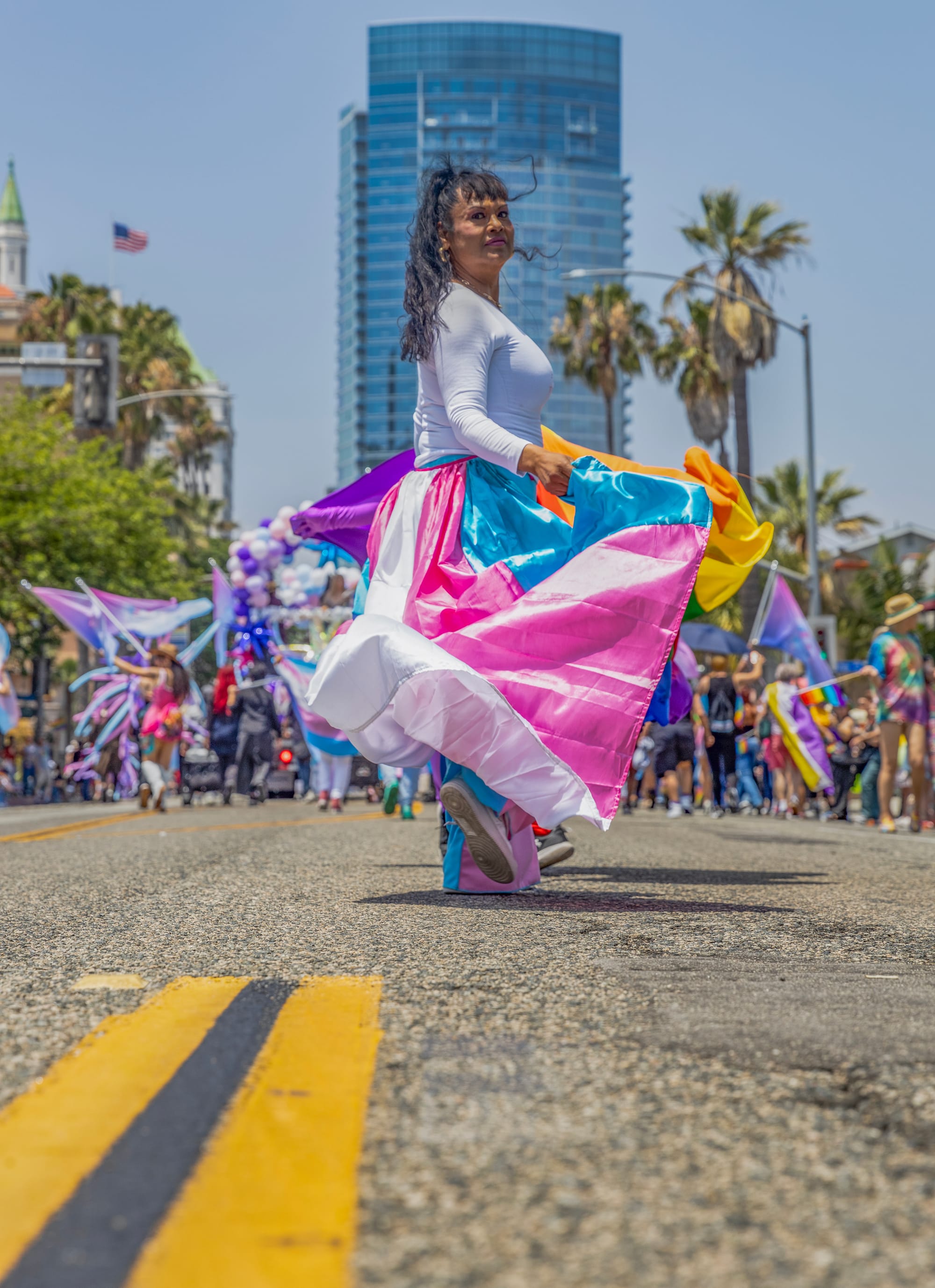 A woman in a colorful pink and blue skirt walks down the street in front of high-rise buildings.