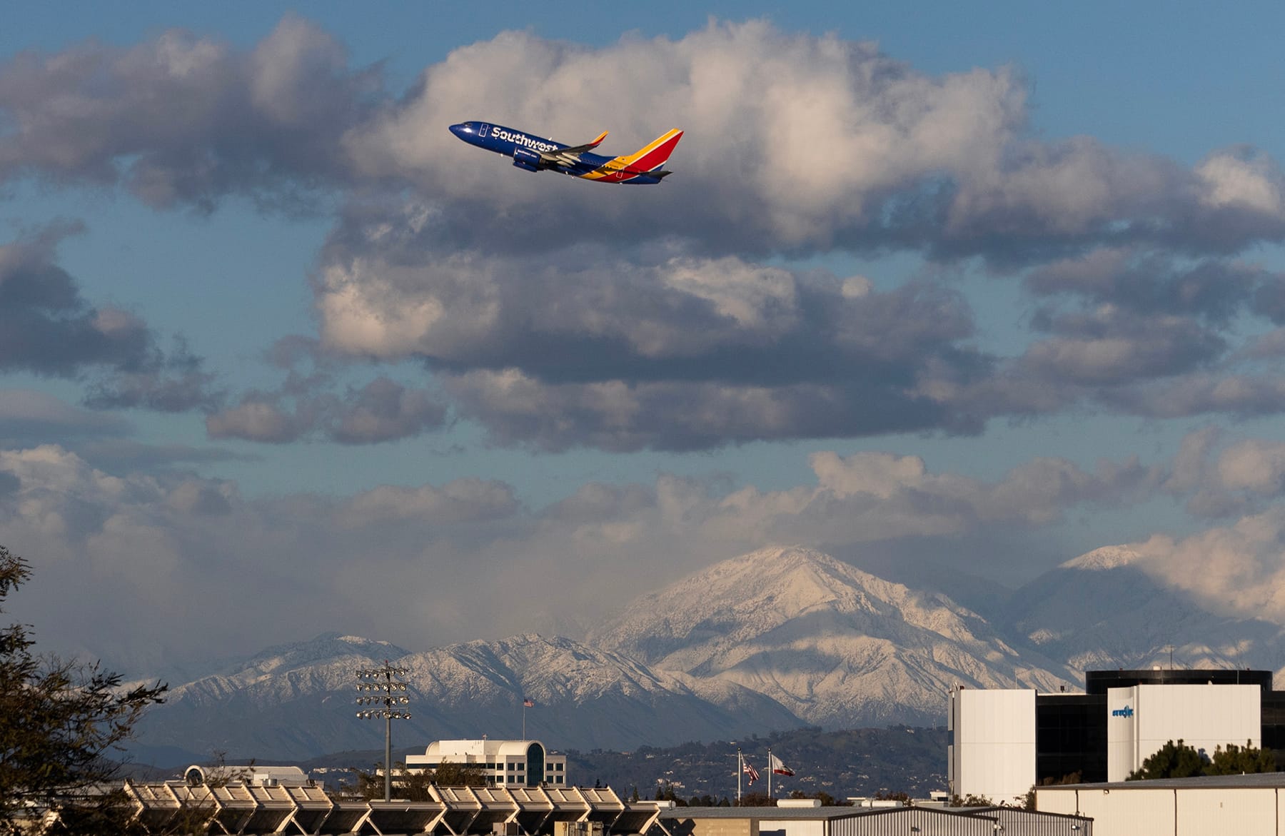 A commercial airliner flies through a cloudy sky over snow-covered mountains.