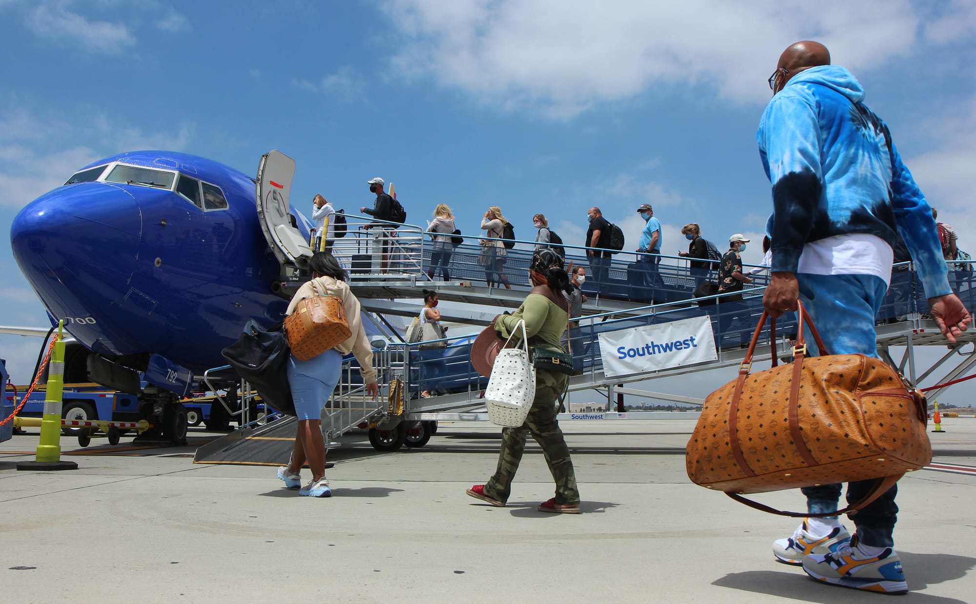 A line of people board a commercial airliner on the ground.