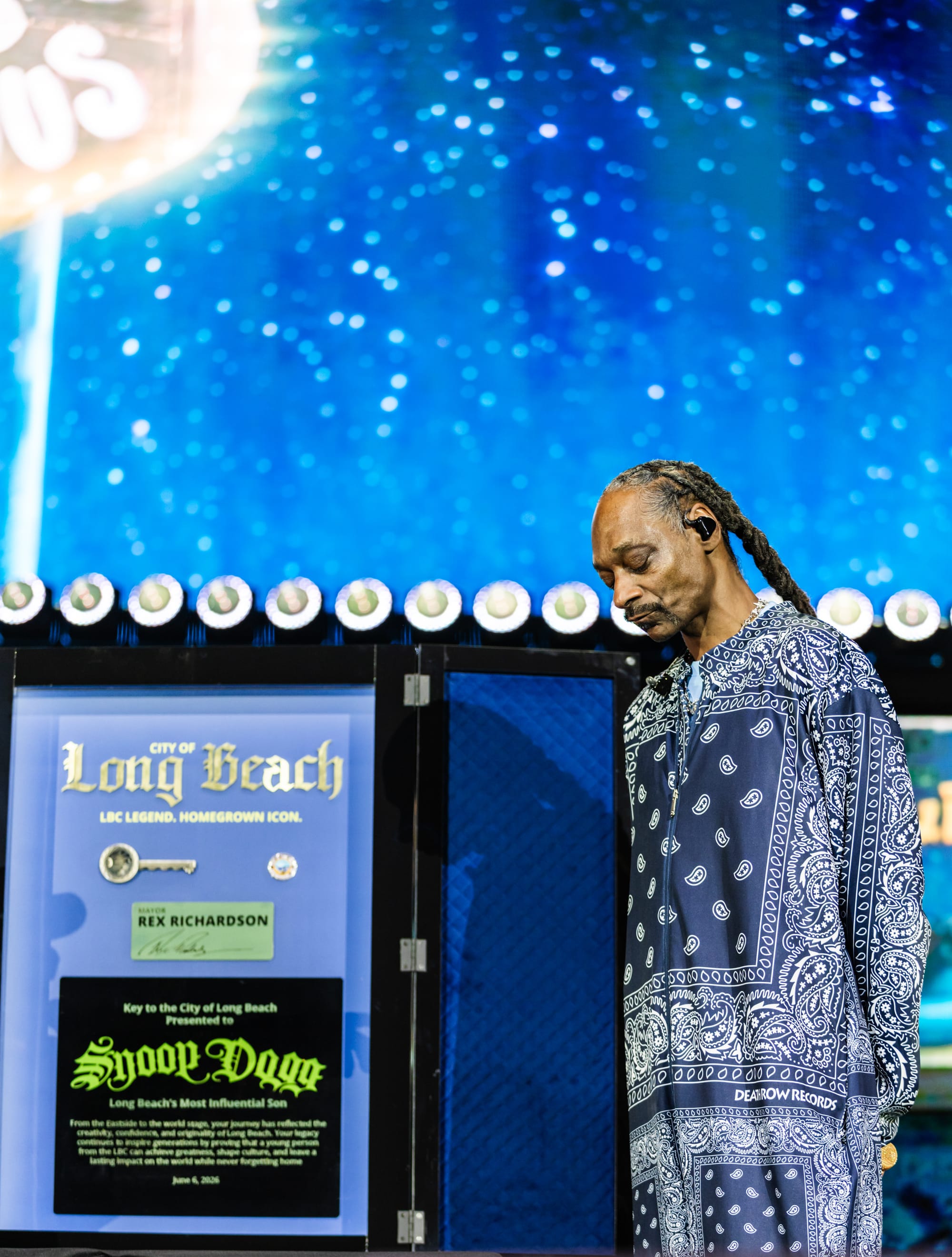 A man in a striking blue outfit stands reverently next to a large display case containing a key and the words "City of Long Beach."