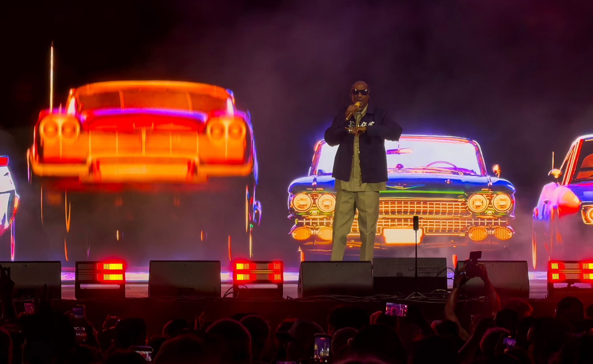 A man stands on stage in front of a four colorful automobiles.