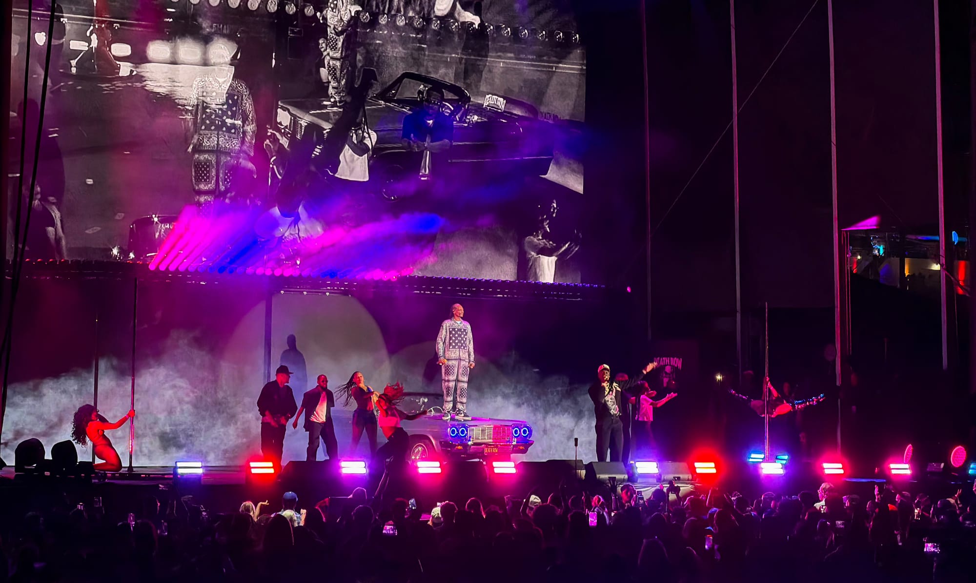 A man stands on stage with other performers at night in front of a large crowd.