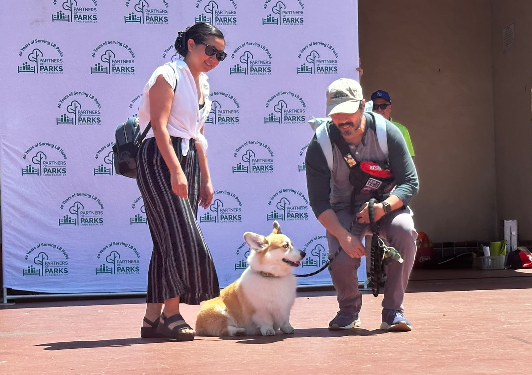 Two people stand on either side of an adorable little dog on a stage.