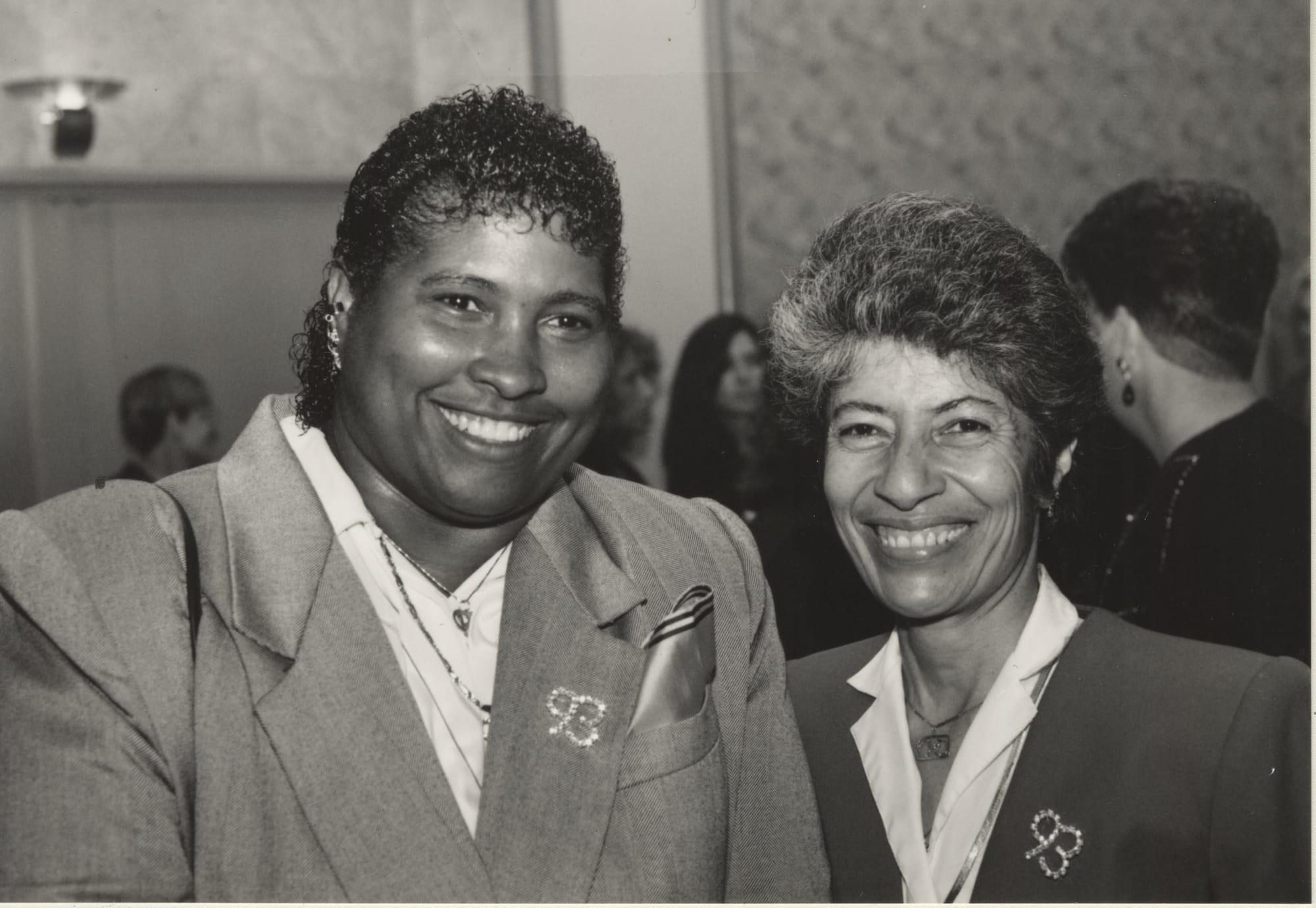 Black and white image of two smiling women standing shoulder to shoulder.