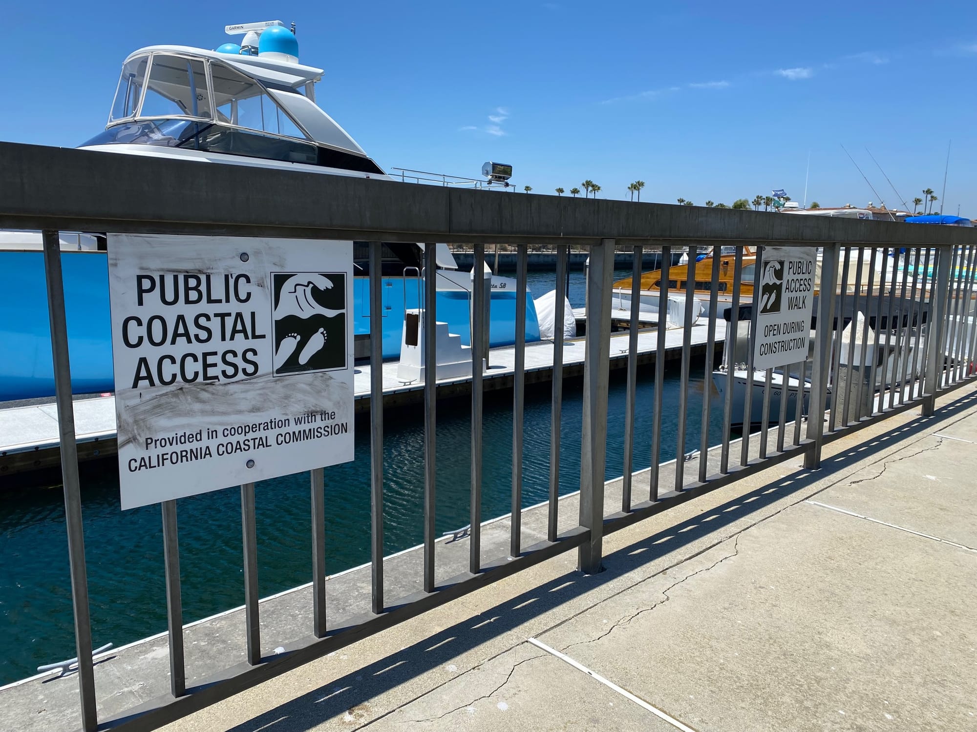 Two signs attached to a metal fence at a marina say "Public Coastal Access" and "Public Access Walk."