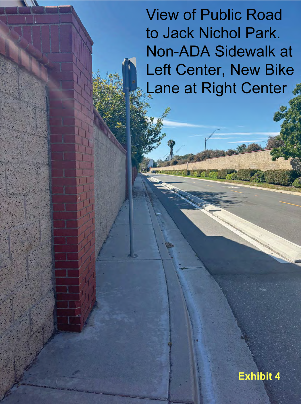 Photo of a narrow sidewalk that has a street sign posted in the middle of it.