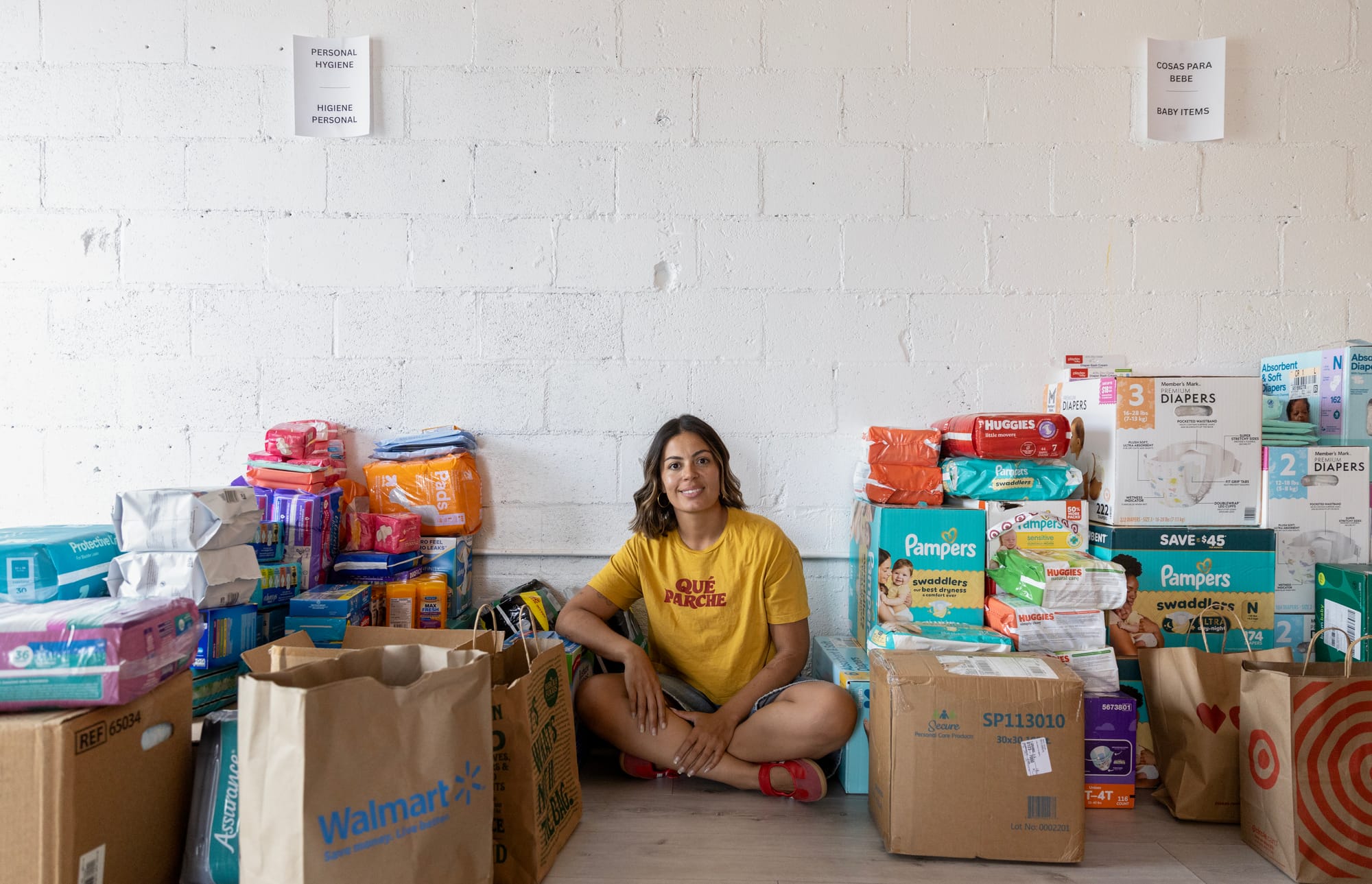 A woman sits crosslegged between multiple bags and boxes of diapers.