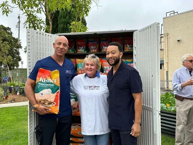 Three people stand outside in front of a large box of pet food bags.