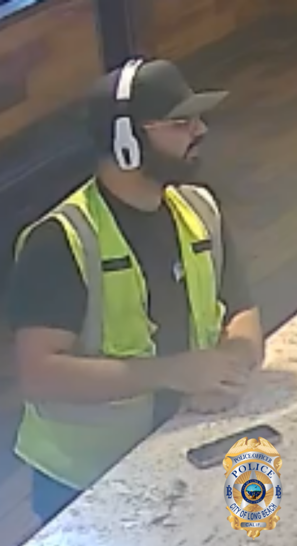 Blurry image of a man bearded man wearing a dark baseball cap, white headphones, black t-shirt, yellow reflective vest and blue pants.