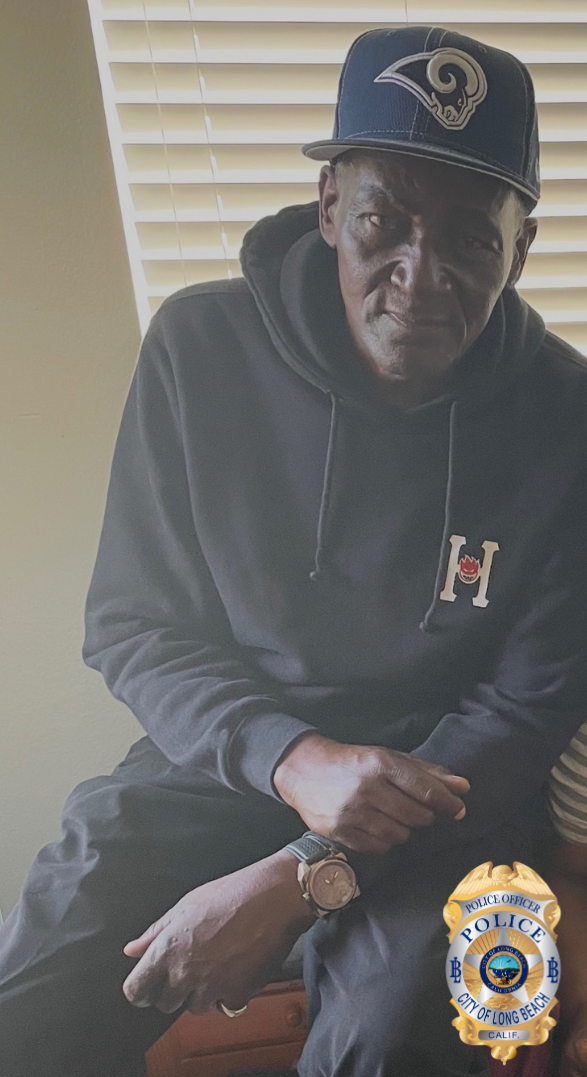 A man wearing a dark hoodie, cap and really nice watch sits on an end table.