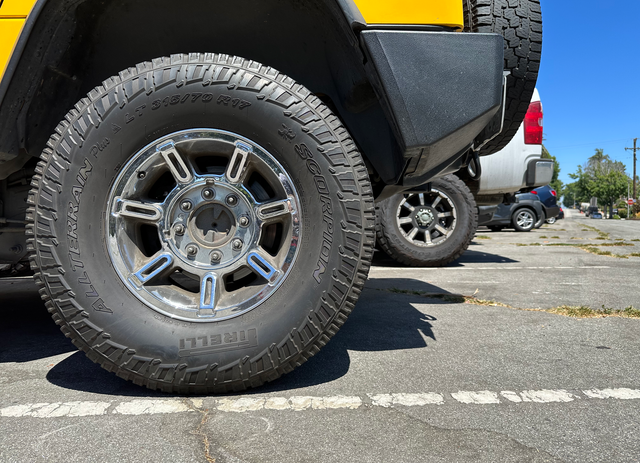 Large tires from several parked vehicles sit on a road with severe cracks and damage.