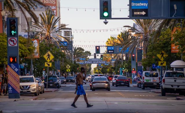 A man in blue shorts and no shirt crosses a busy city street.