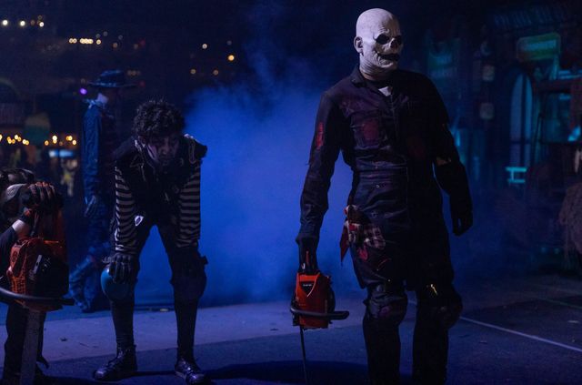 Men in scary costumes and masks stand in a dark, foggy area.