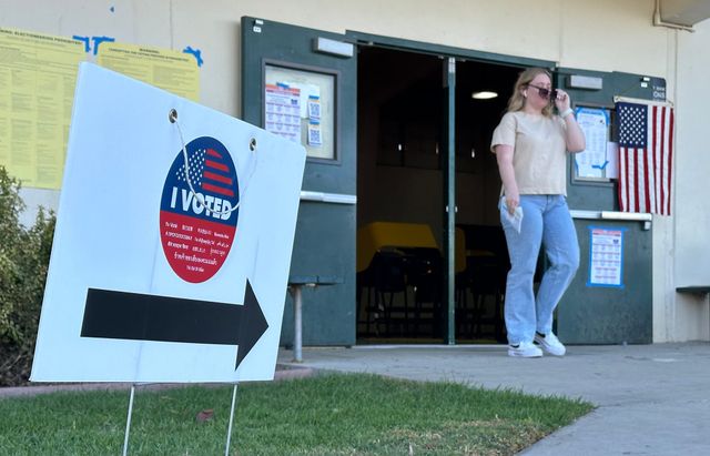 A woman puts on sunglasses as she walks out of a building next to a sign saying “I voted.