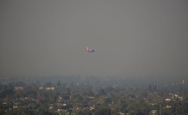 A plane flies though a murky brown sky.