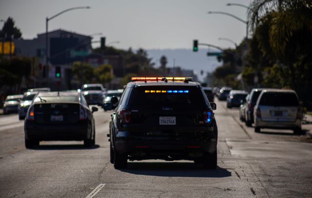 A police SUV with yellow, red and blue lights flashing drives down the street.