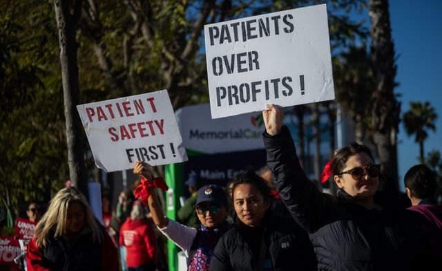 People stand outside holding signs that say "Patient safety first!" and "Patients over profits!"