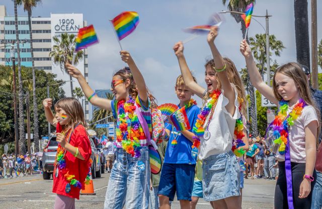 Five children wear rainbow colors and wave rainbow flags.