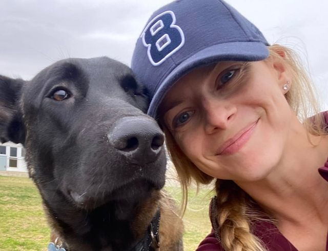 A woman in a blue baseball cap touches her head to a sweet black dog's head.