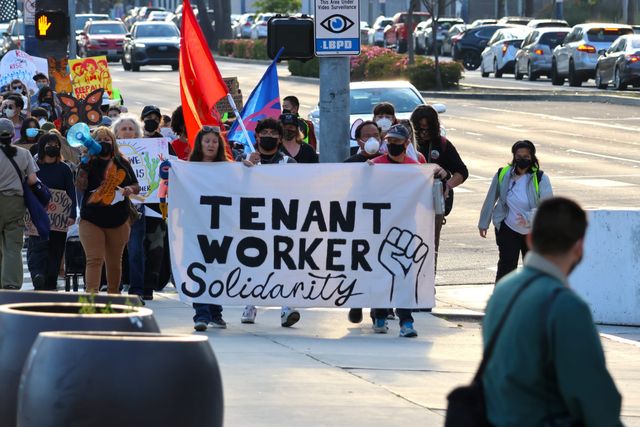People walk on a street behind a banner reading "Tenant Worker Solidarity.