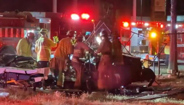Firefighters in uniform work on a wrecked car at night.