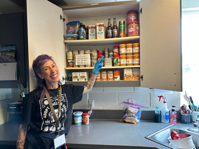 A woman points to a pantry full of jars, bottles and cans of food.