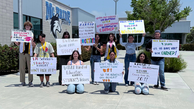 A group of young people stand in front of a building labeled "McBride Pride" while holding up hand-written signs.