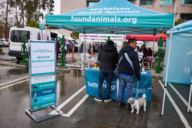 Two people and a small dog stand under a tent labeled "Michelson Found Animals foundanimals.org."