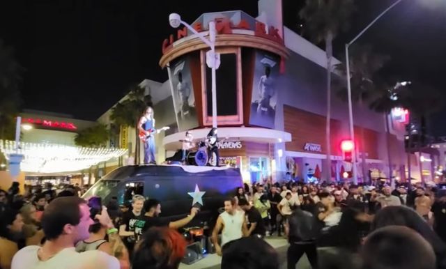 A crowd surrounds a band on a van at a street corner at night.