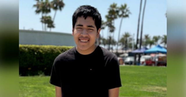 A smiling teenage boy in a black shirt stands on green grass.