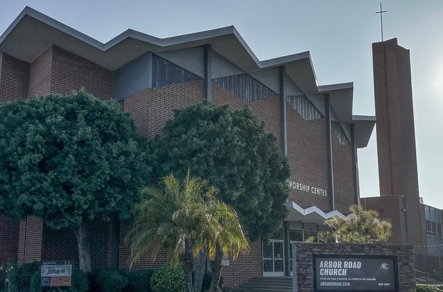 A large brown building next to three trees and a sign saying "Arbor Road Church."